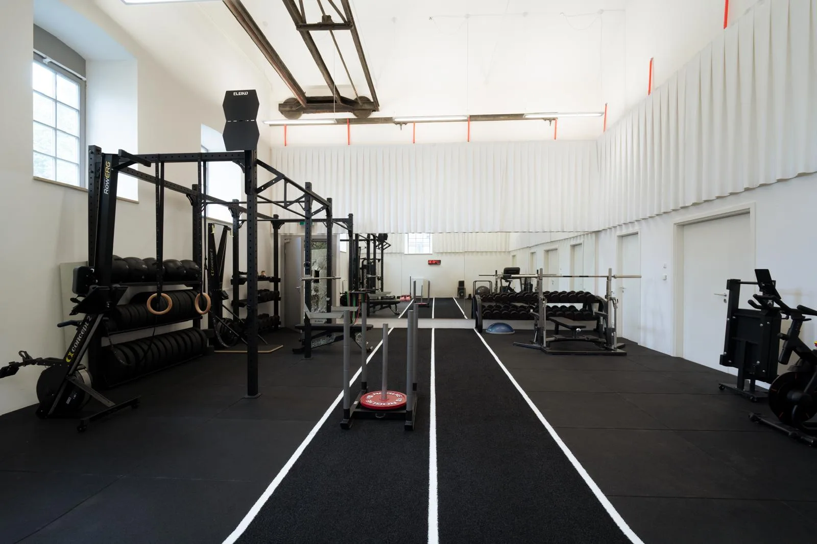 Weite Trainingshalle mit Laufbahn, Racks und Freihanteln